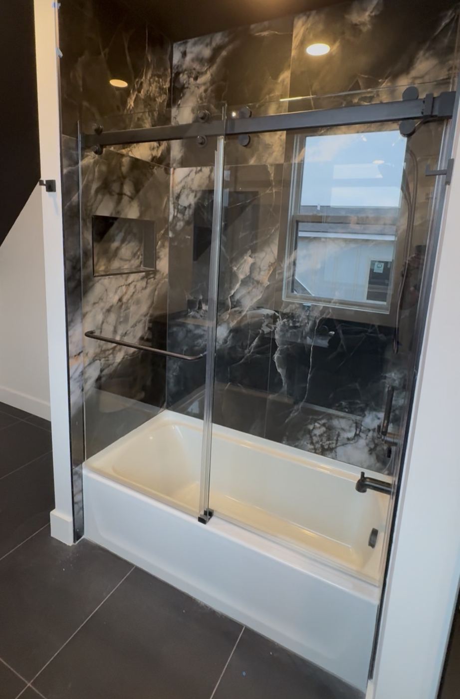 Frameless sliding tub door in front of black marble walls