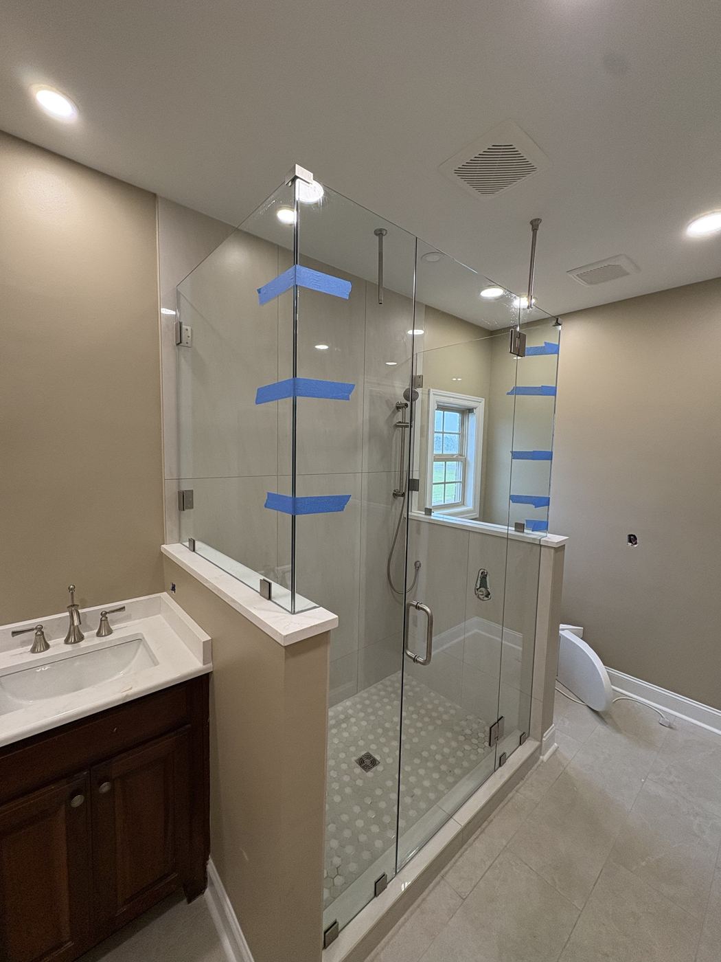 Frameless shower on a half wall with ceiling support bars, brushed nickel